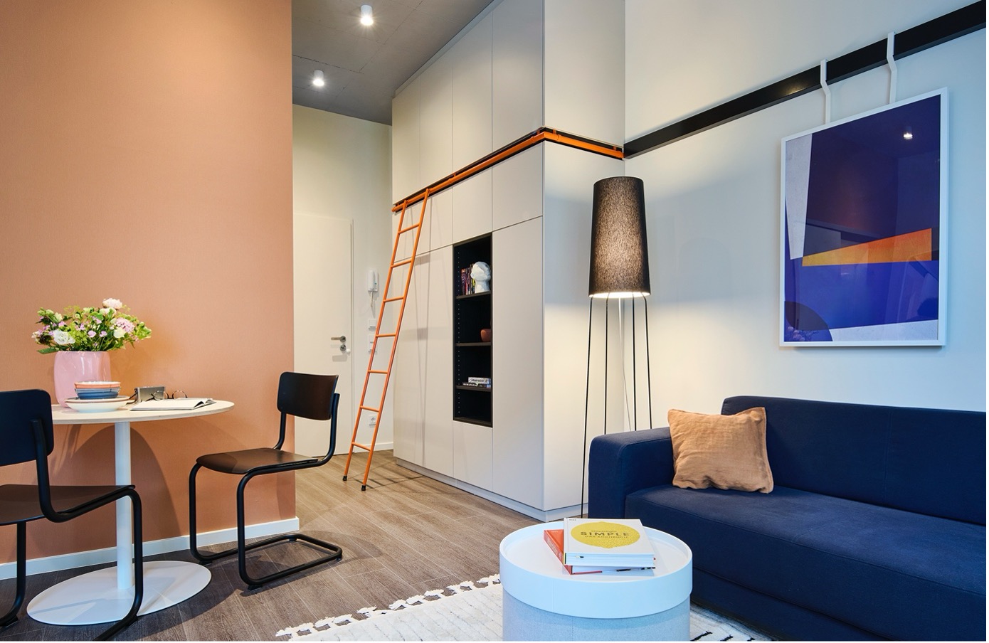 Modernes Mikroapartment-Interieur mit blauem Sofa, Pfirsichwand und orangefarbener Leiter